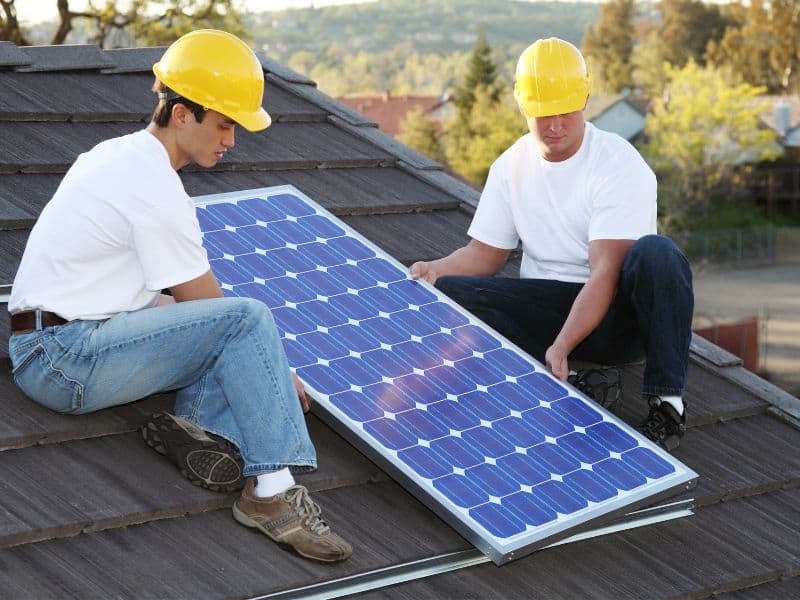 Two men wearing yellow hard hats holding and installing a solar panel on a rooftop